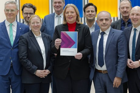 Gruppenbild: B&auml;rbel Bas (SPD), Bundesministerin f&uuml;r Arbeit und Soziales, h&auml;lt den Abschlussbericht der Kommission zur Sozialstaatsreform in die Kamera. Die Mitglieder der Kommission stehen um sie herum.