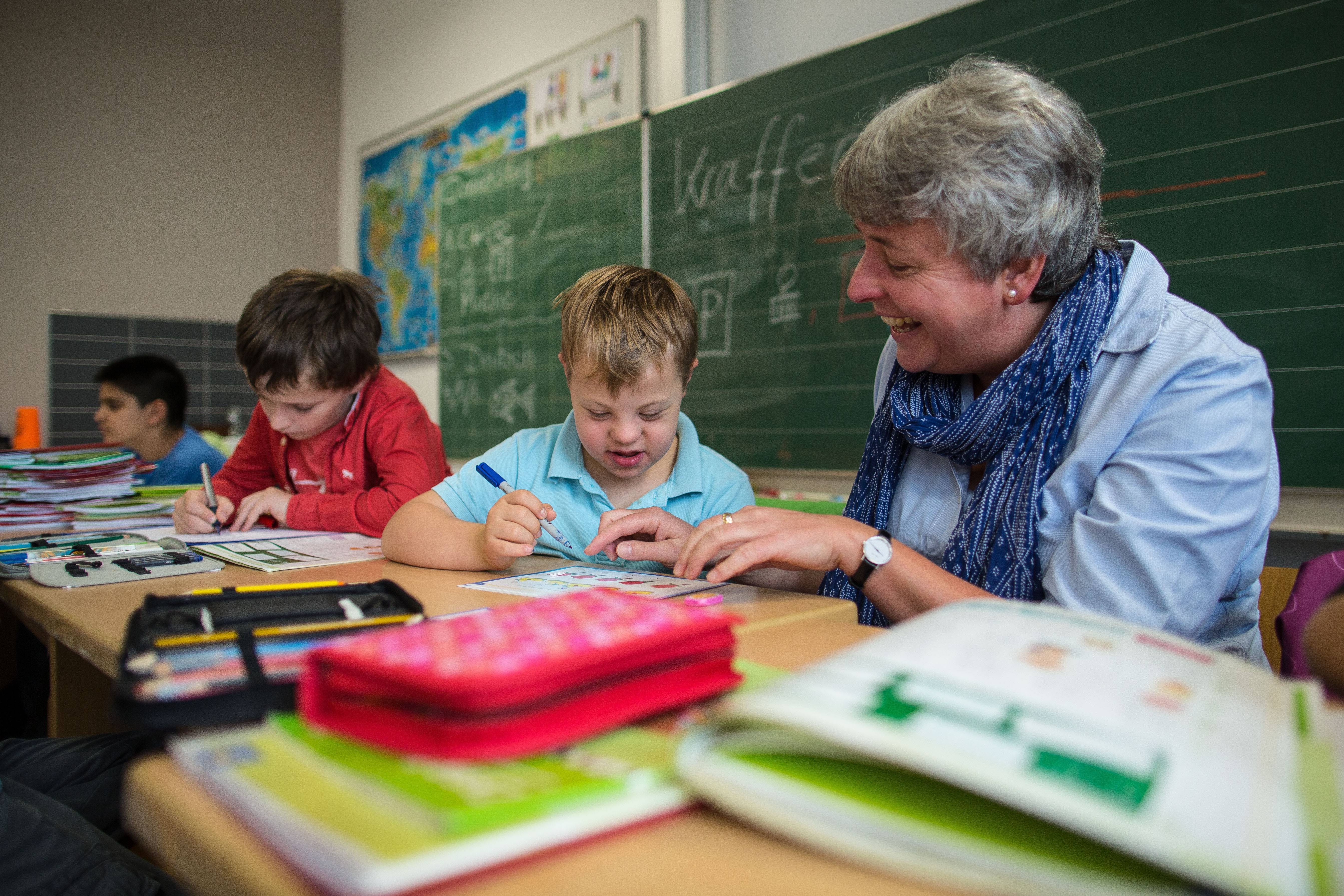Inklusives Lernen in der Schule Blick in eine Schulklasse, eine Inklusionshelferin kümmert sich um einen Jungen mit Trisomie 21.