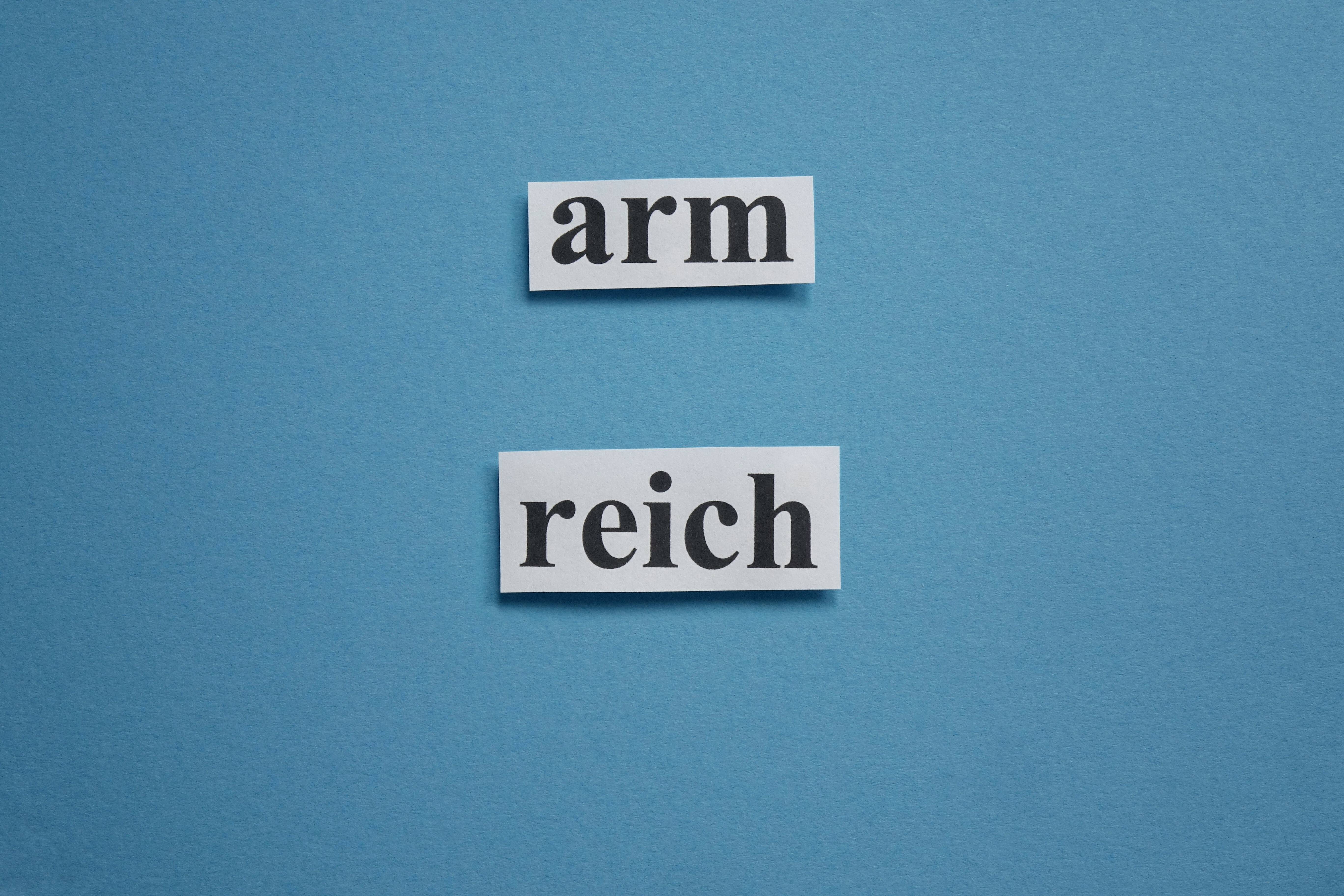 Ungleiche Vermögensverteilung Auf blauem Grund stehen die Wörter "arm" und "reich" aus ausgeschnittenem Papier