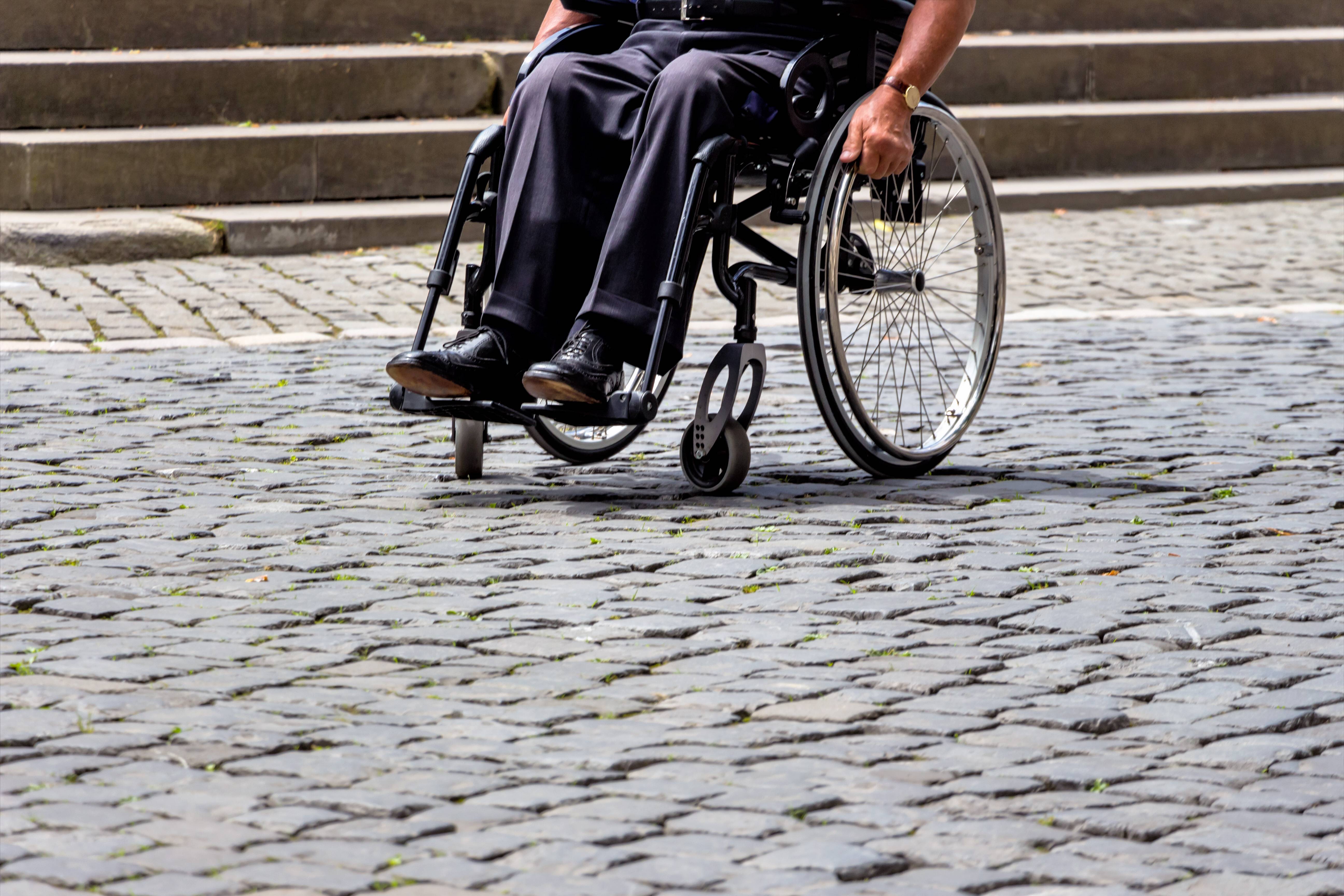 Mann im Rollstuhl auf einem gepflasterten Weg vor einer Treppe 