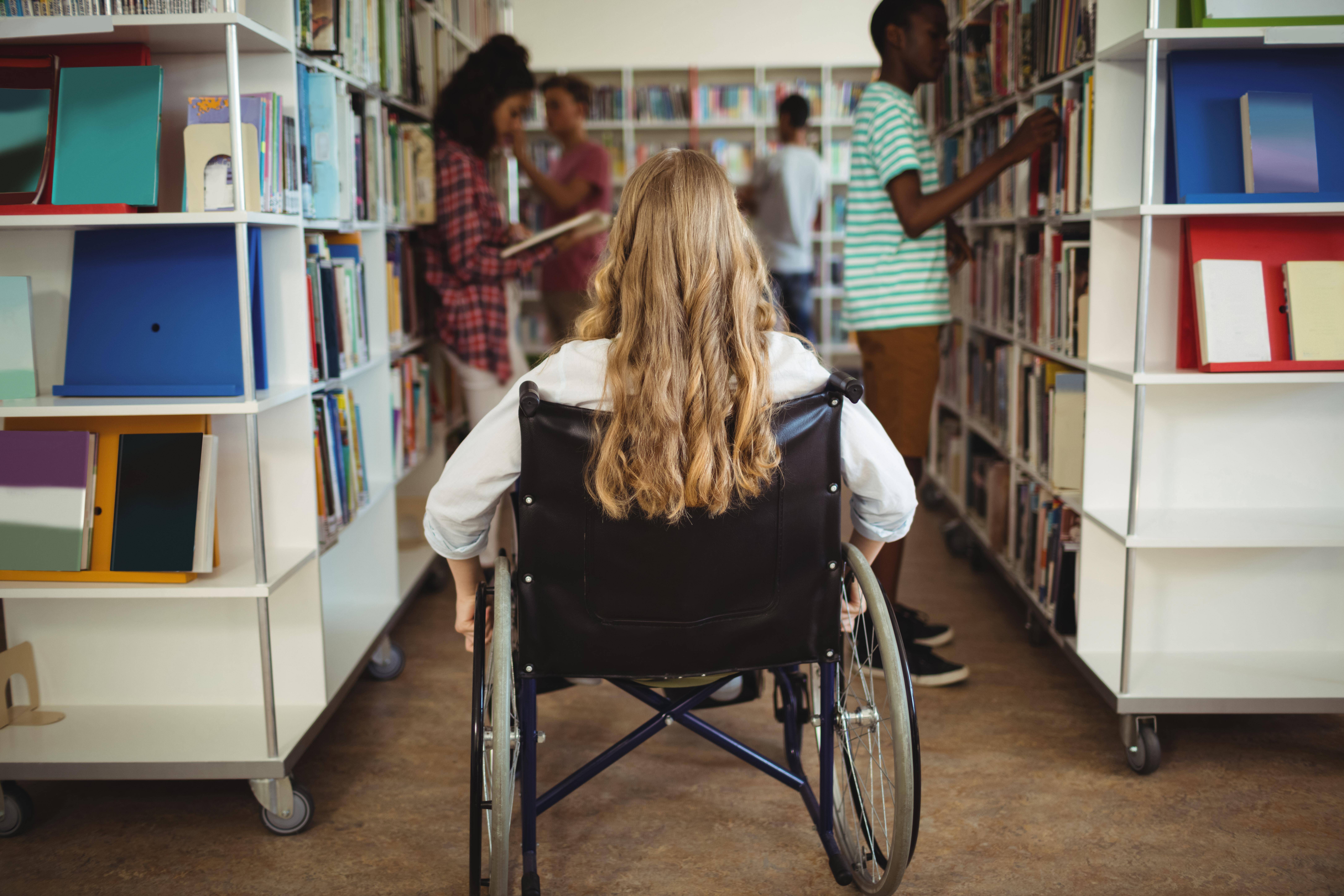 Junge Frau im Rollstuhl Junge Frau sitzt in einem Rollstuhl. Sie befindet sich in einer Bibliothek.
