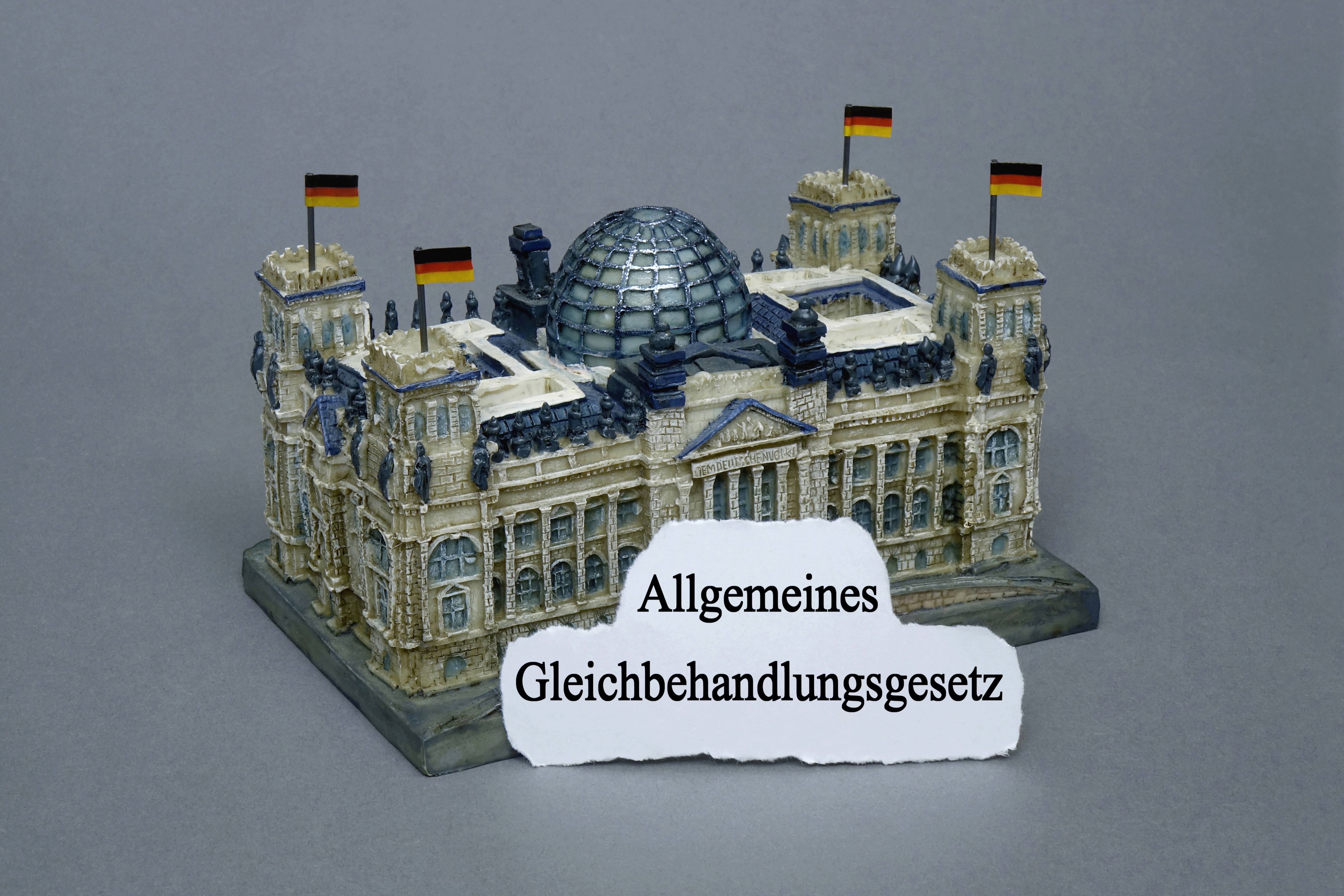 Bildmontage: Miniatur-Reichstag mit dem Schriftzug "Allgemeines Gleichbehandlungsgesetz"