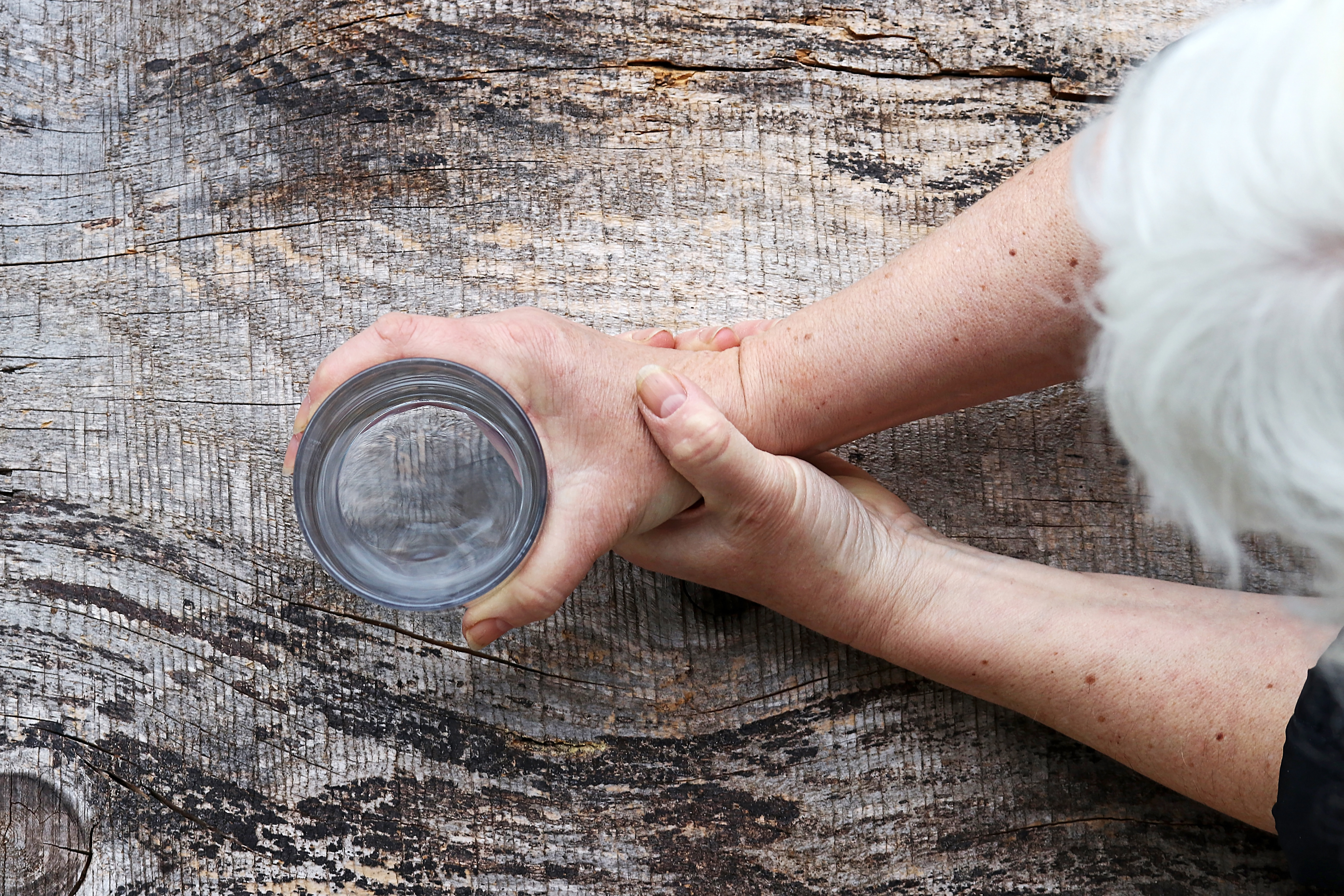Bild aus Vogelperspektive: Eine ältere Dame hält mit der einen Hand ein Wasserglas, mit der anderen Hand hält sie beides fest.