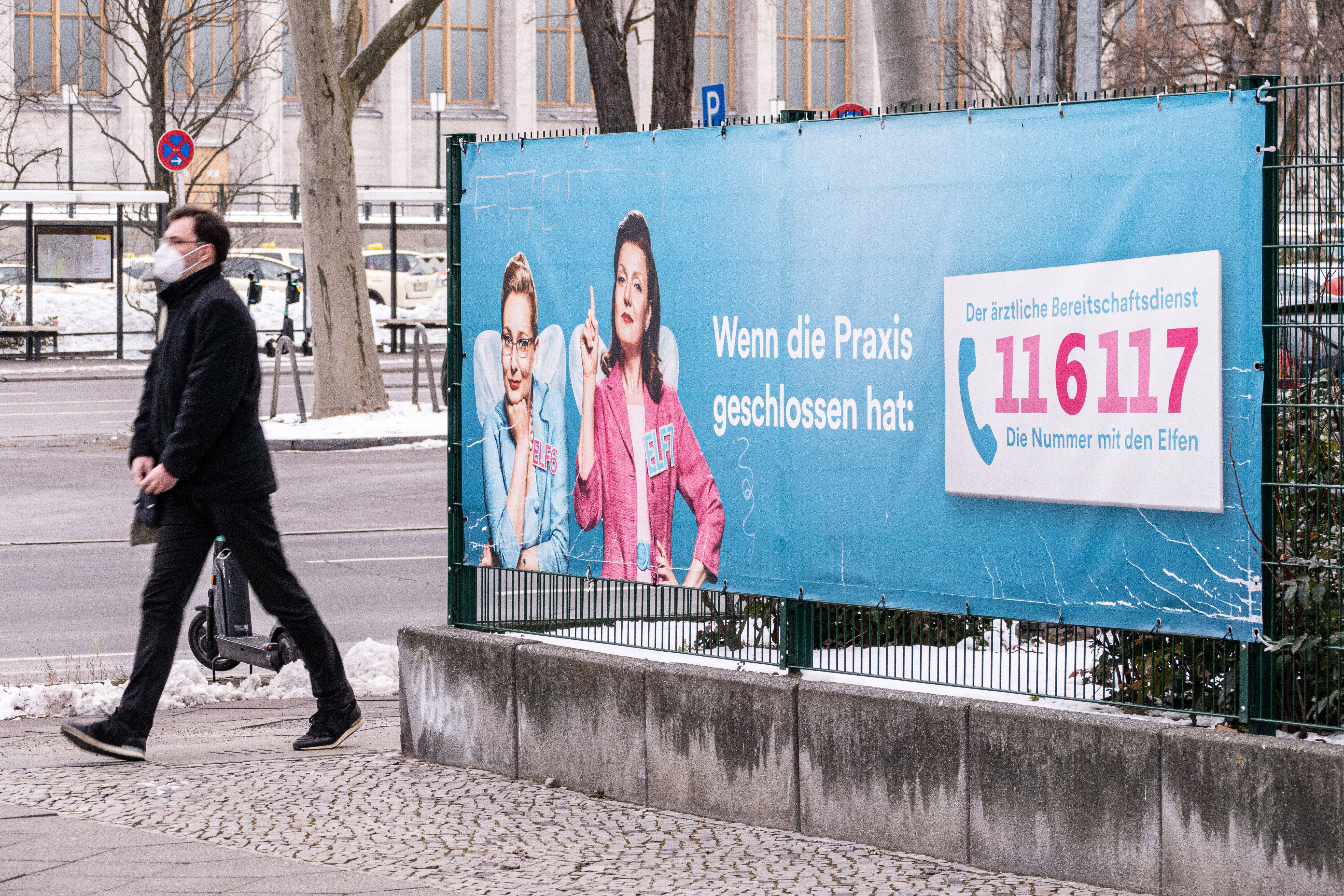 Bereitschaftsdienst 116117 Ein Plakat, das für den ärztlichen Bereitschaftsdienst 116 117 wirbt; ein Passant läuft vorbei.