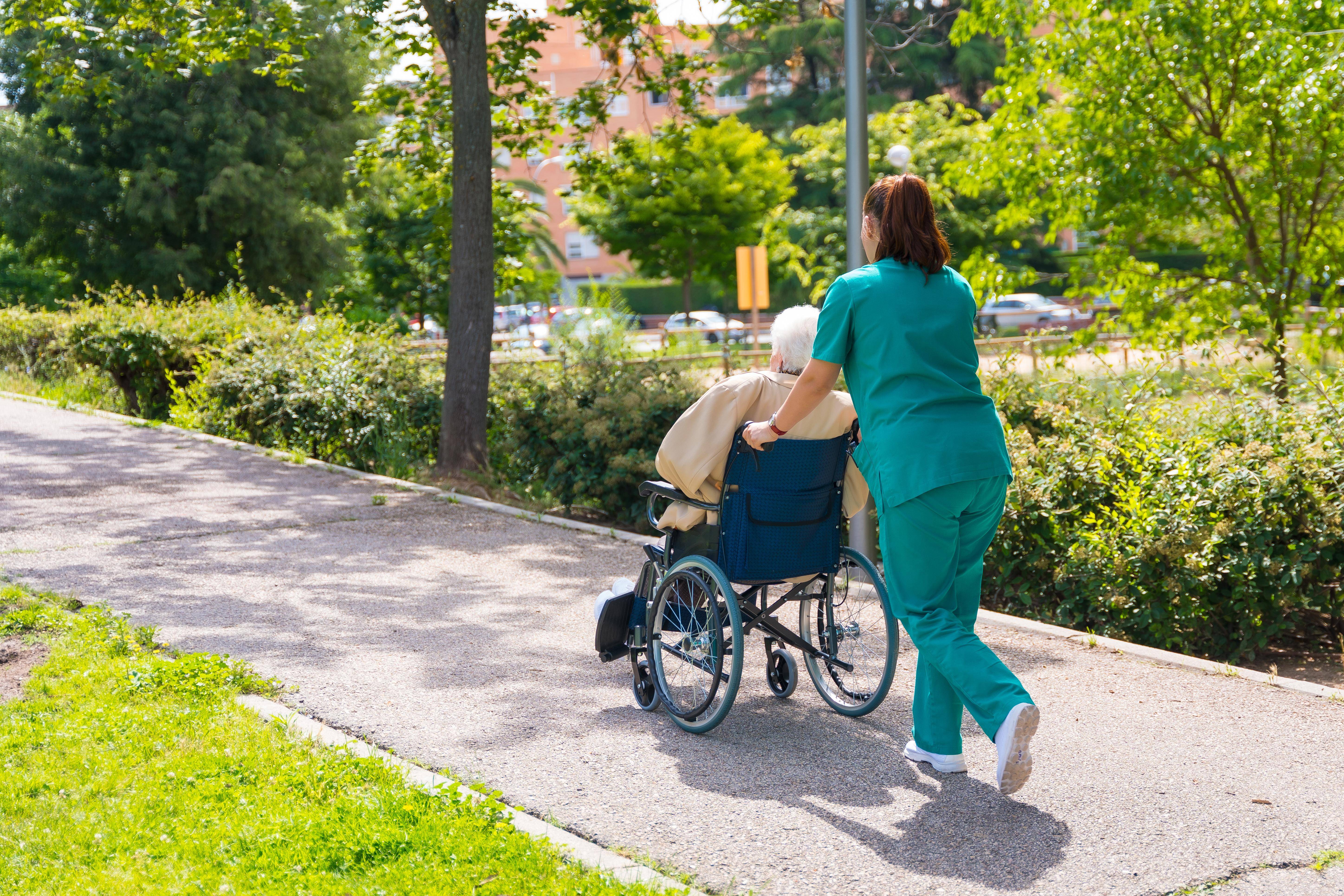 Krankenpflegerin schiebt alte Frau im Rollstuhl