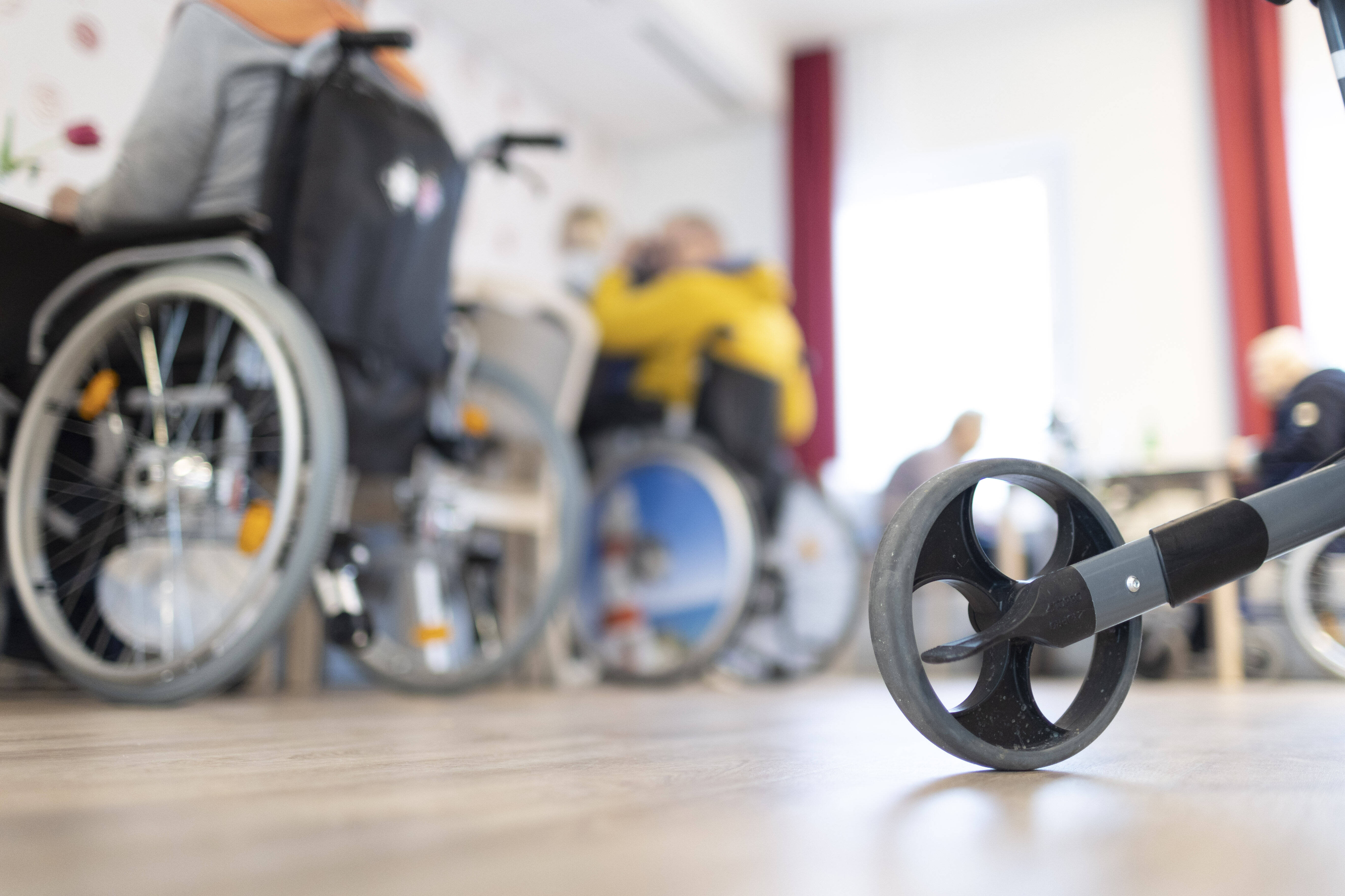 Pflegeheim Blick in einen Raum in einem Pflegeheim, mehrere Menschen mit Rollstühlen sitzen an Tischen, im Vordergrund sieht man ein Rad eines Rollators