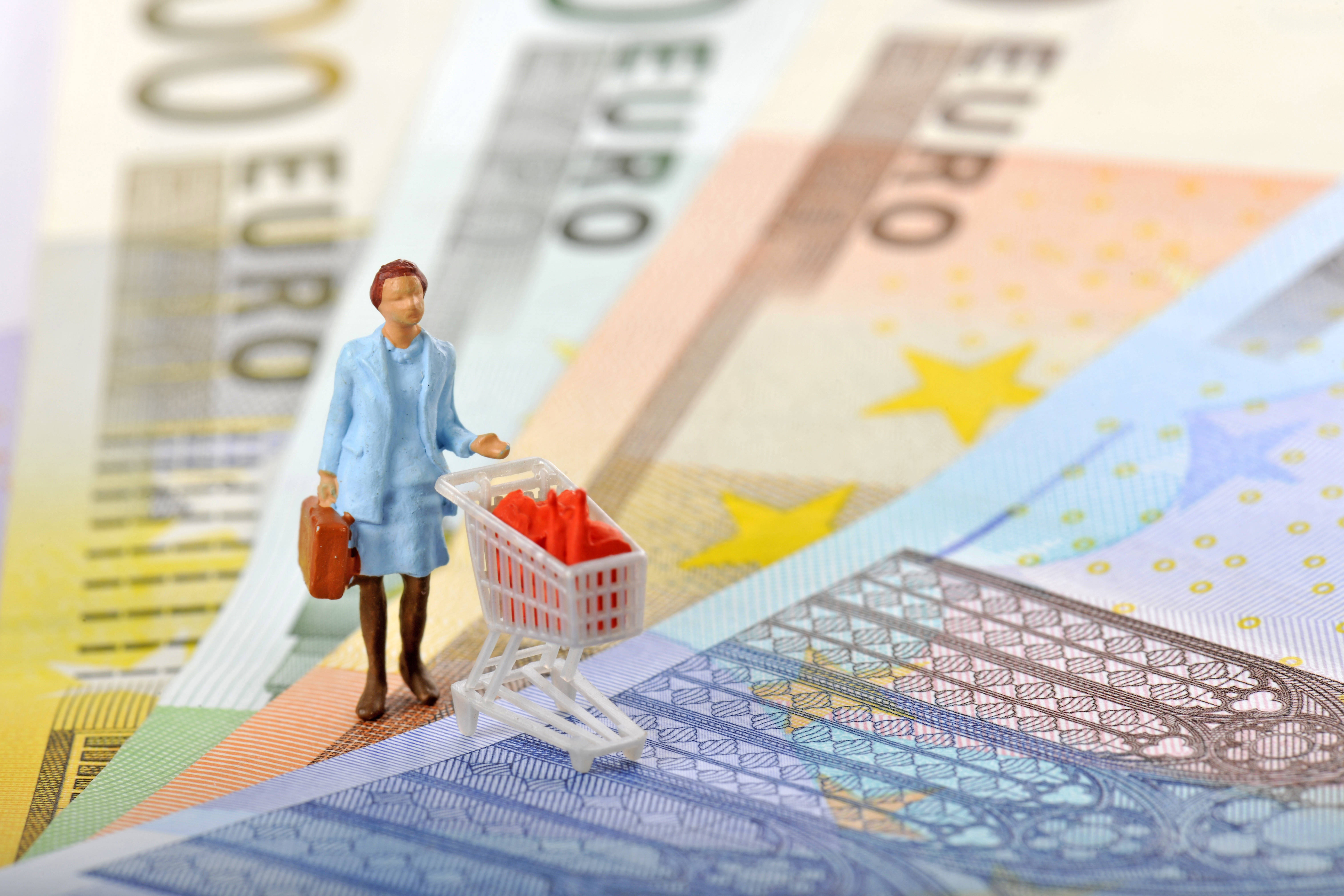 Anstieg der Inflation bei Lebensmitteln Plastikfigur einer alten Frau schiebt einen Einkaufwagen. Sie steht auf diversen Euro-Scheinen.