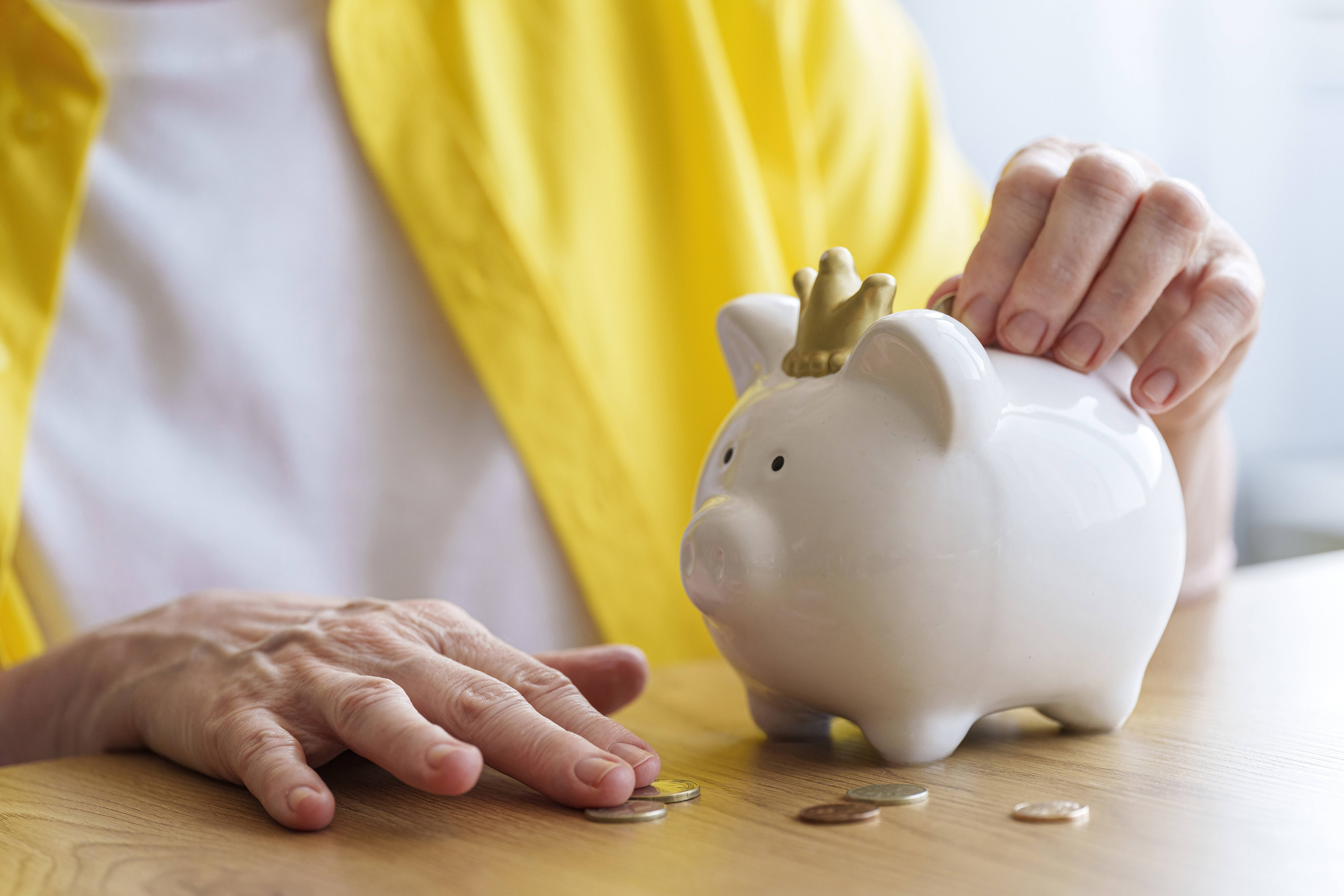 Rentenerhöhung Eine ältere Frau steckt Geld in ein Sparschwein