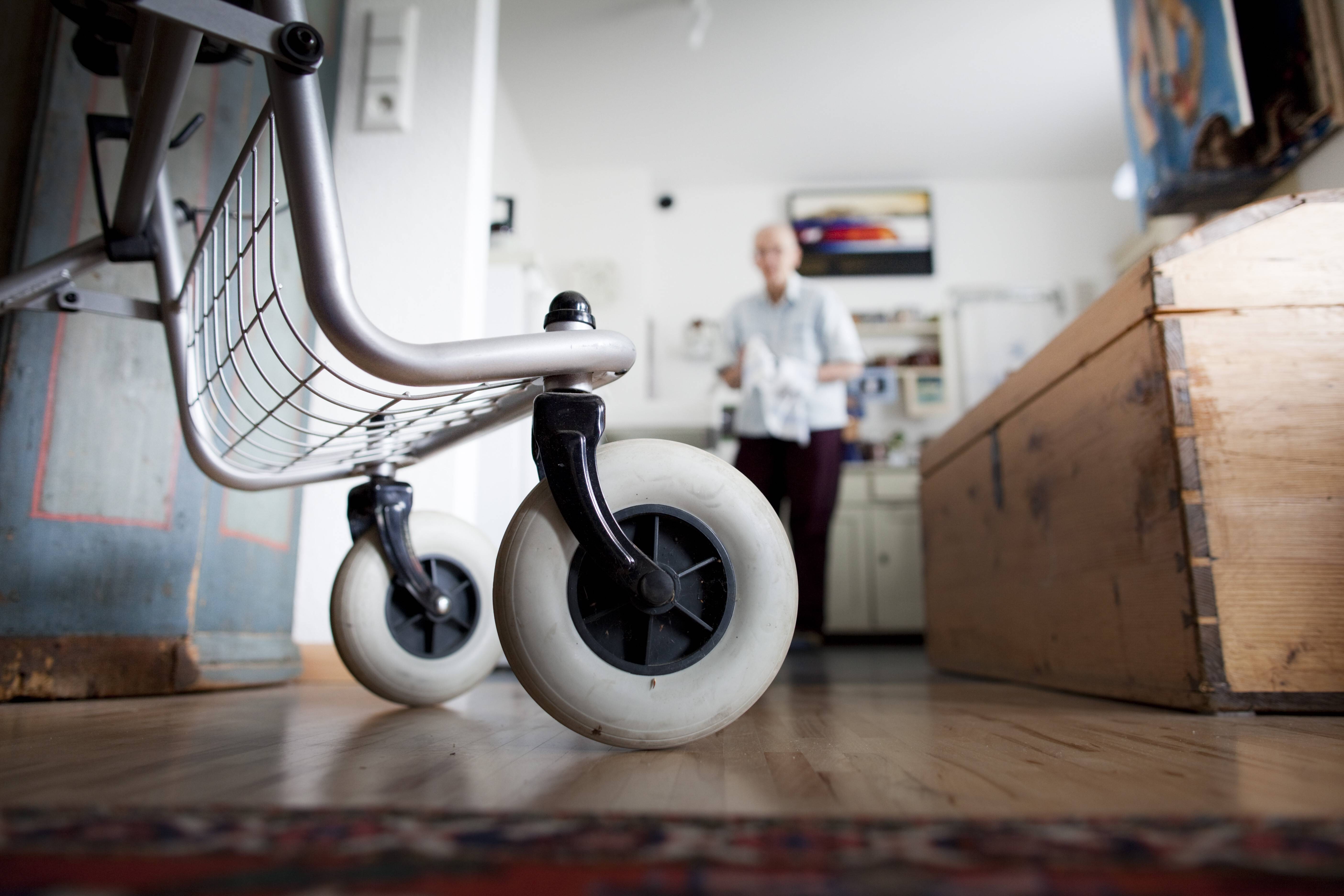 Blick in eine Küche, man sieht die Räder eines Rollators im Vordergrund, im Hintergrund verschwommen ein älterer Mann.