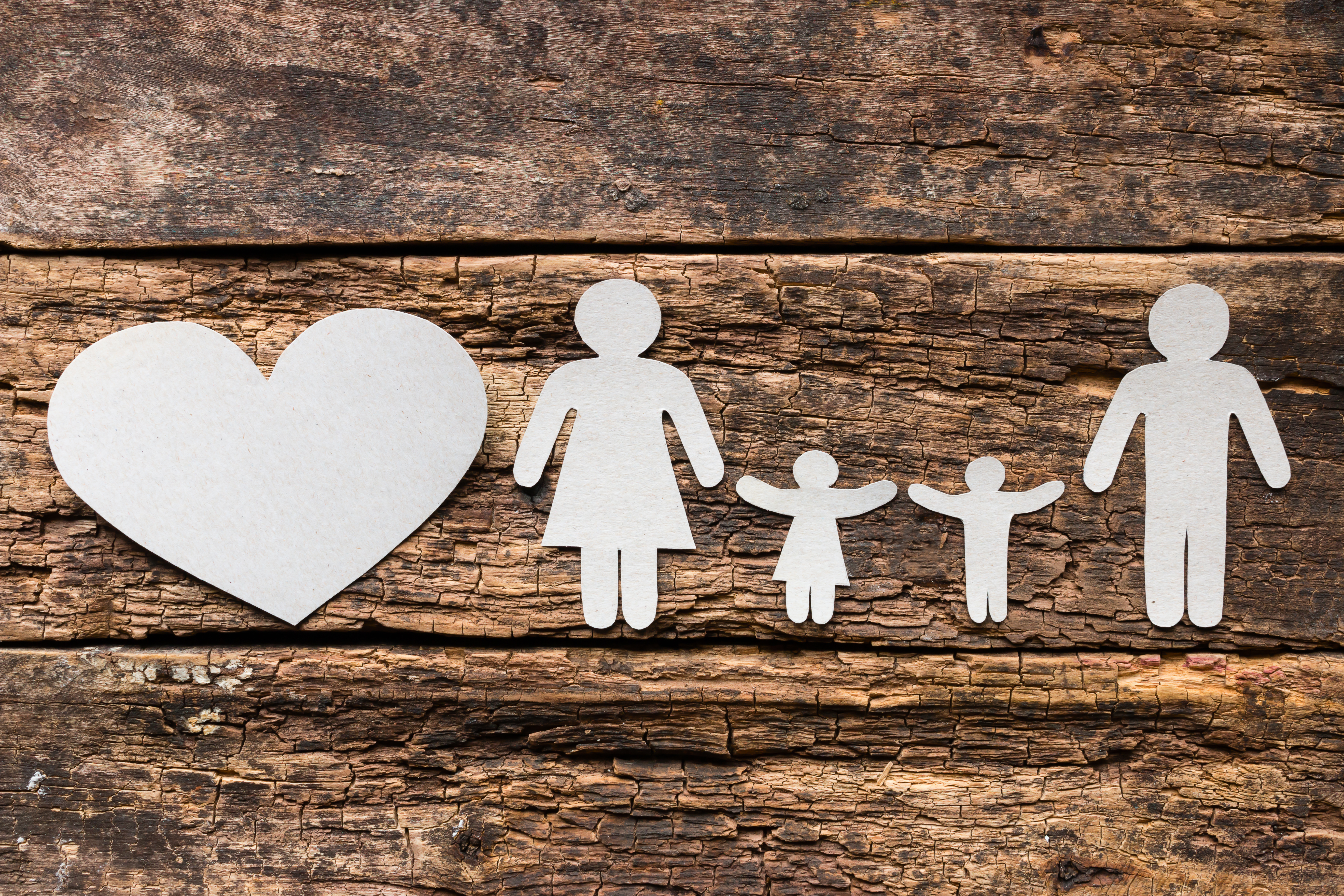 Eine aus Papier ausgeschnittene Familie mit Vater, Mutter und zwei Kindern auf h&ouml;lzernem Untergrund