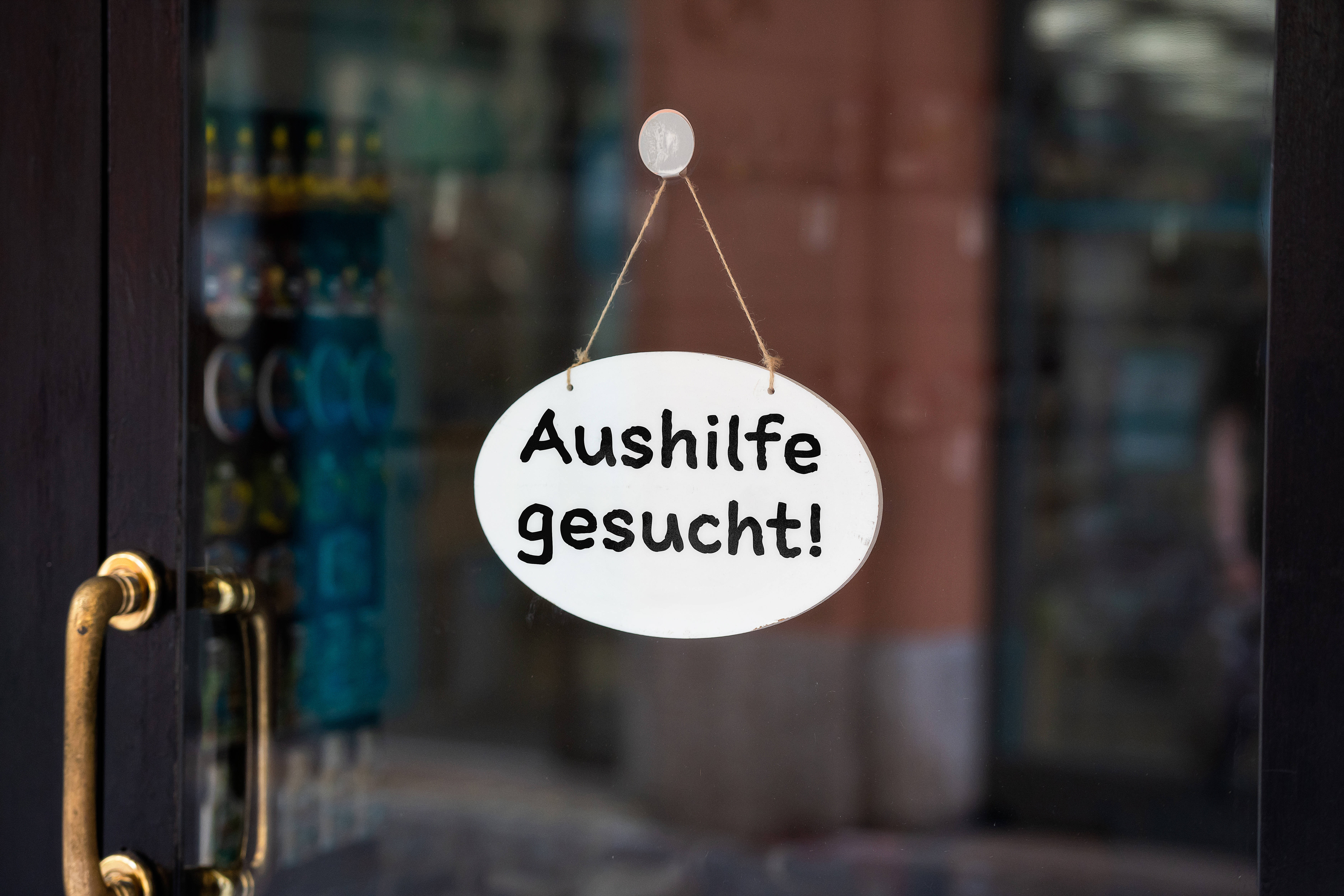 Aushilfe gesucht Glastür, an der innen ein Schild angebracht ist mit der Aufschrift "Aushilfe gesucht!"