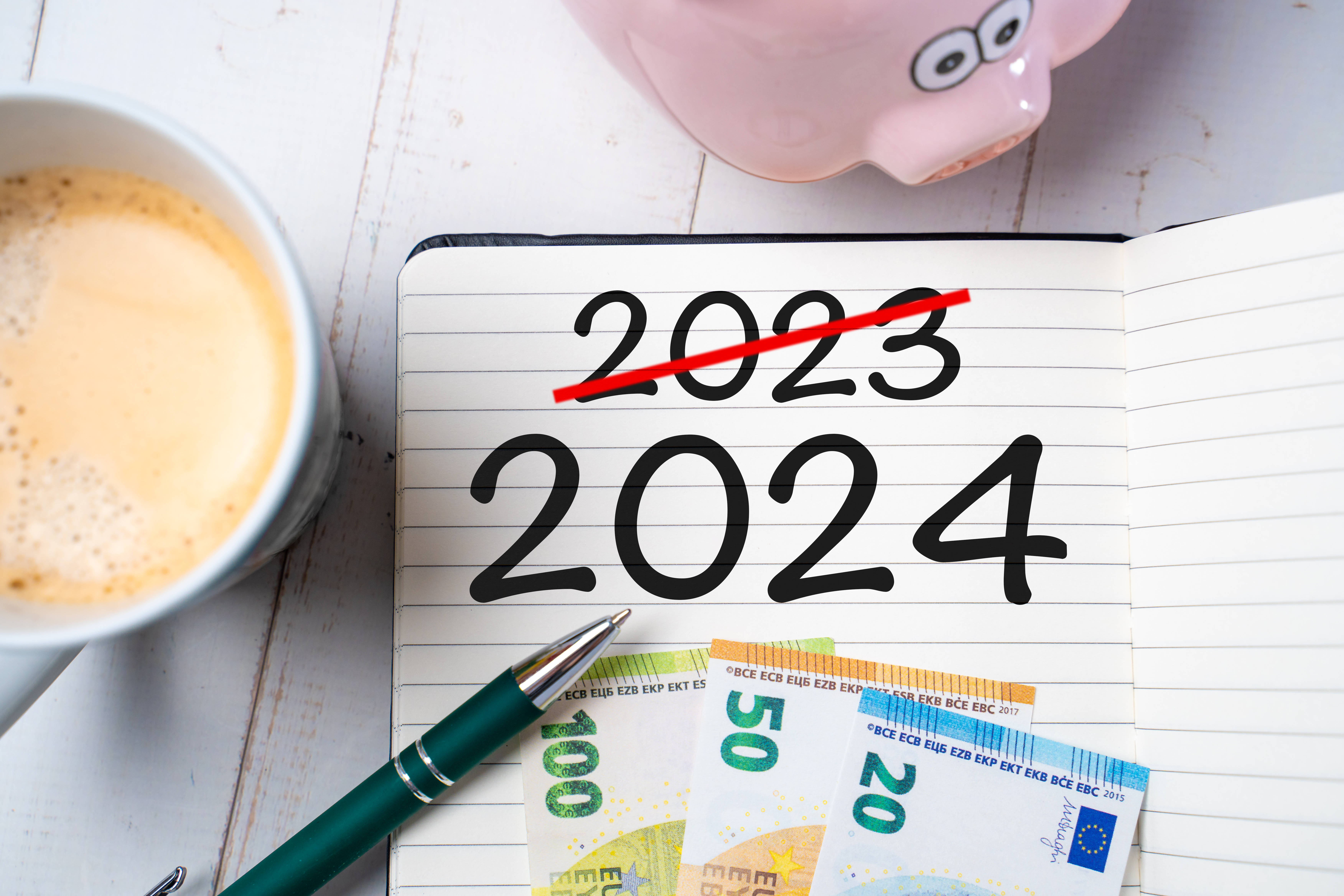 Änderungen in 2024 Ein Notizblock mit der Zahl 2024 und einer durchgestrichenen Zahl 2023 auf einem Schreibtisch zusammen mit einem Sparschwein und Euroscheinen.