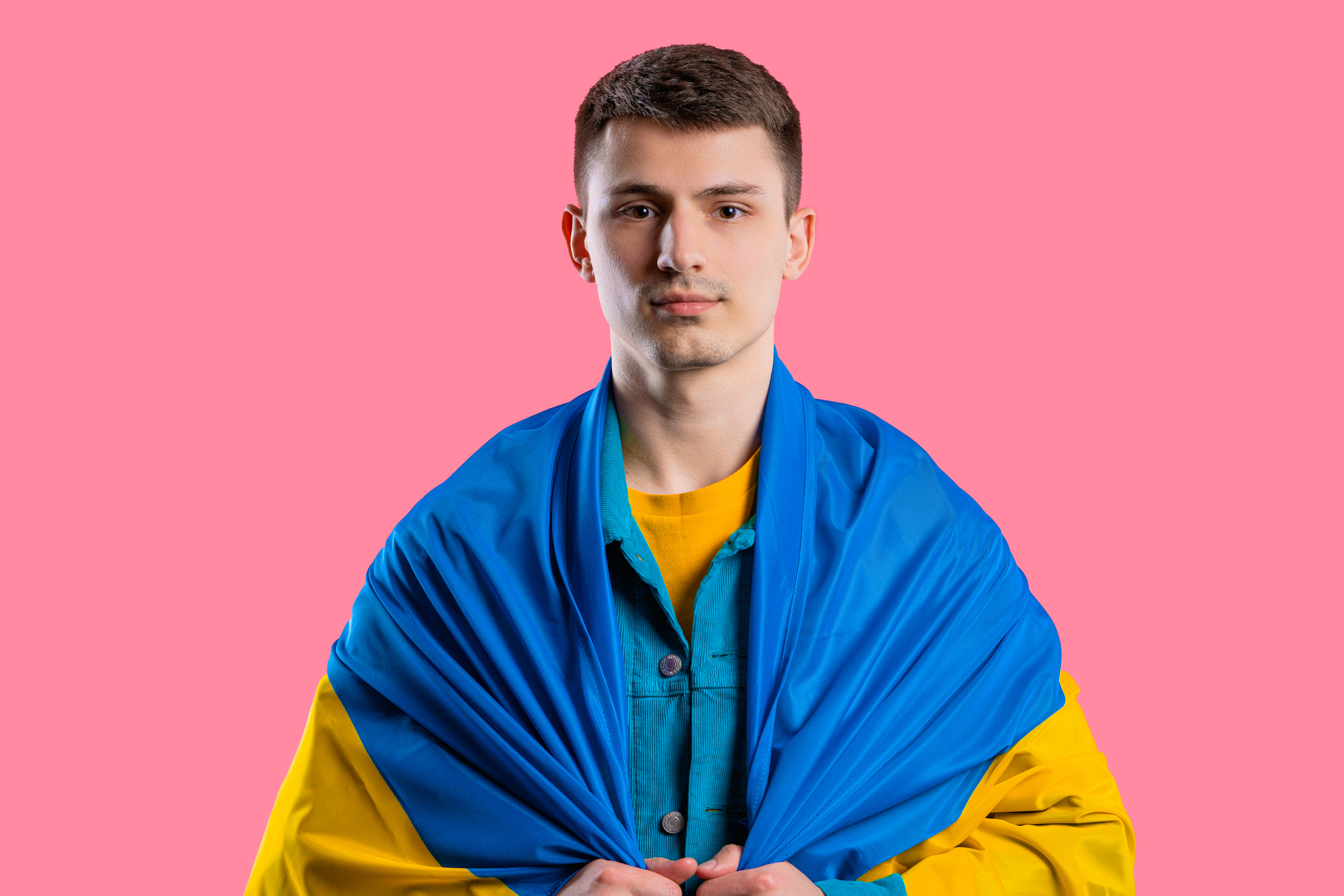 Jugendlicher mit ukrainischer Flagge Ein junger Mann schaut in die Kamera, er trägt eine ukrainische Landesflagge um die Schultern gelegt