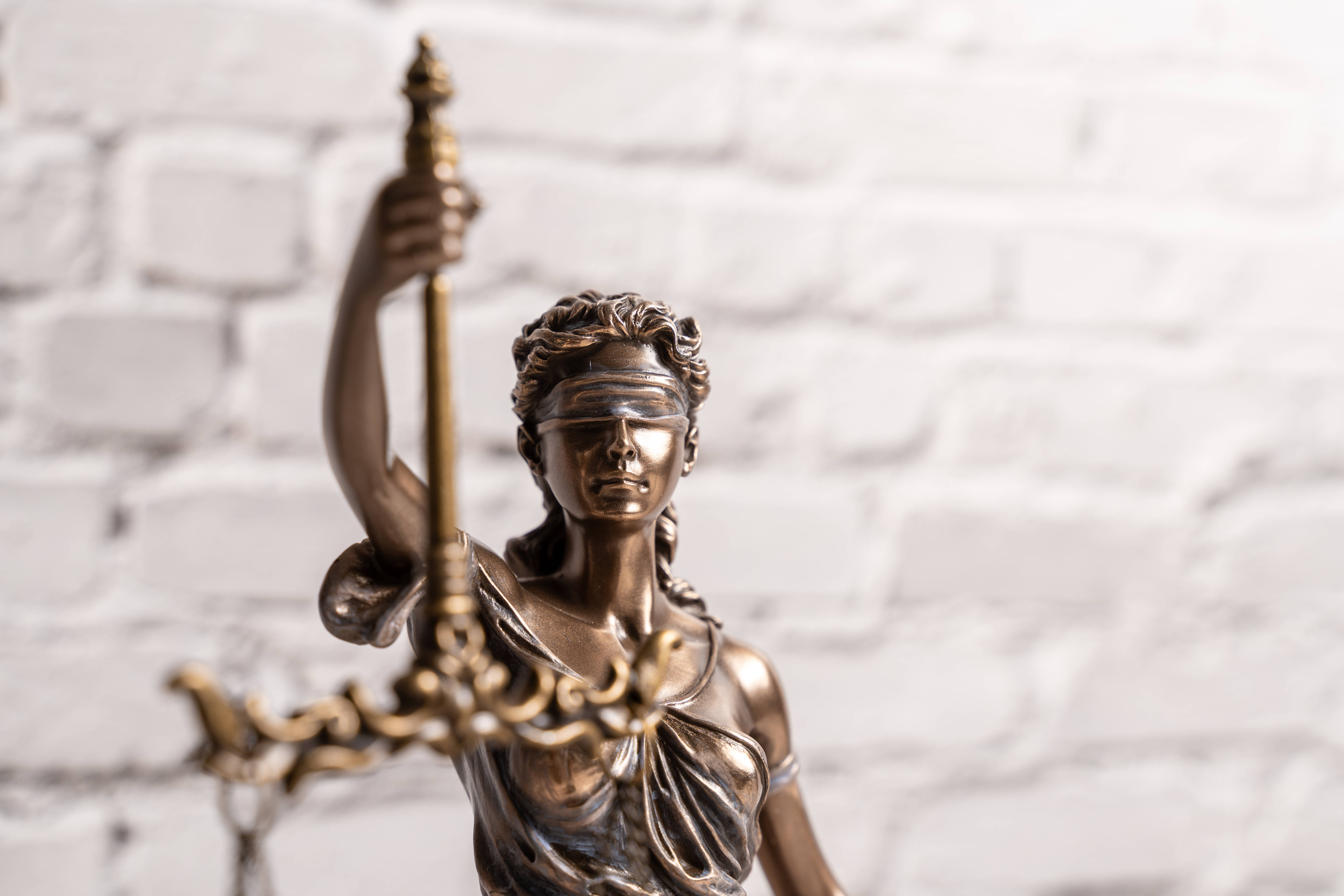 Eine bronzene Statue der Justitia vor einer gemauerten weißen Wand