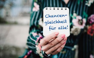 Block mit der Aufschrift "Chancengleichheit für alle" wird von einer Frauenhand in die Kamera gehalten