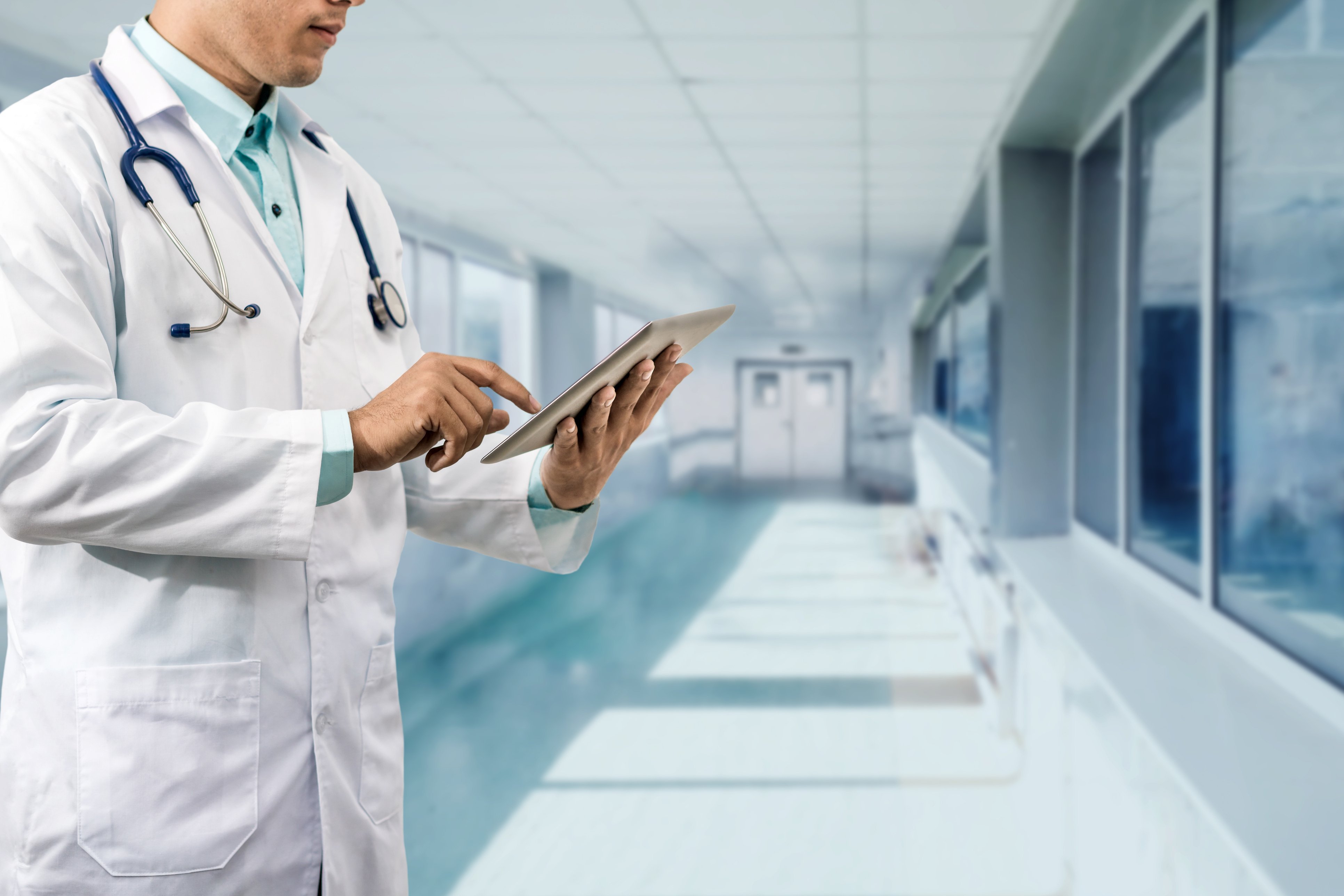 Arzt in Krankenhausflur mit Tablet beim Abrufen einer elektronischen Patientenakte.