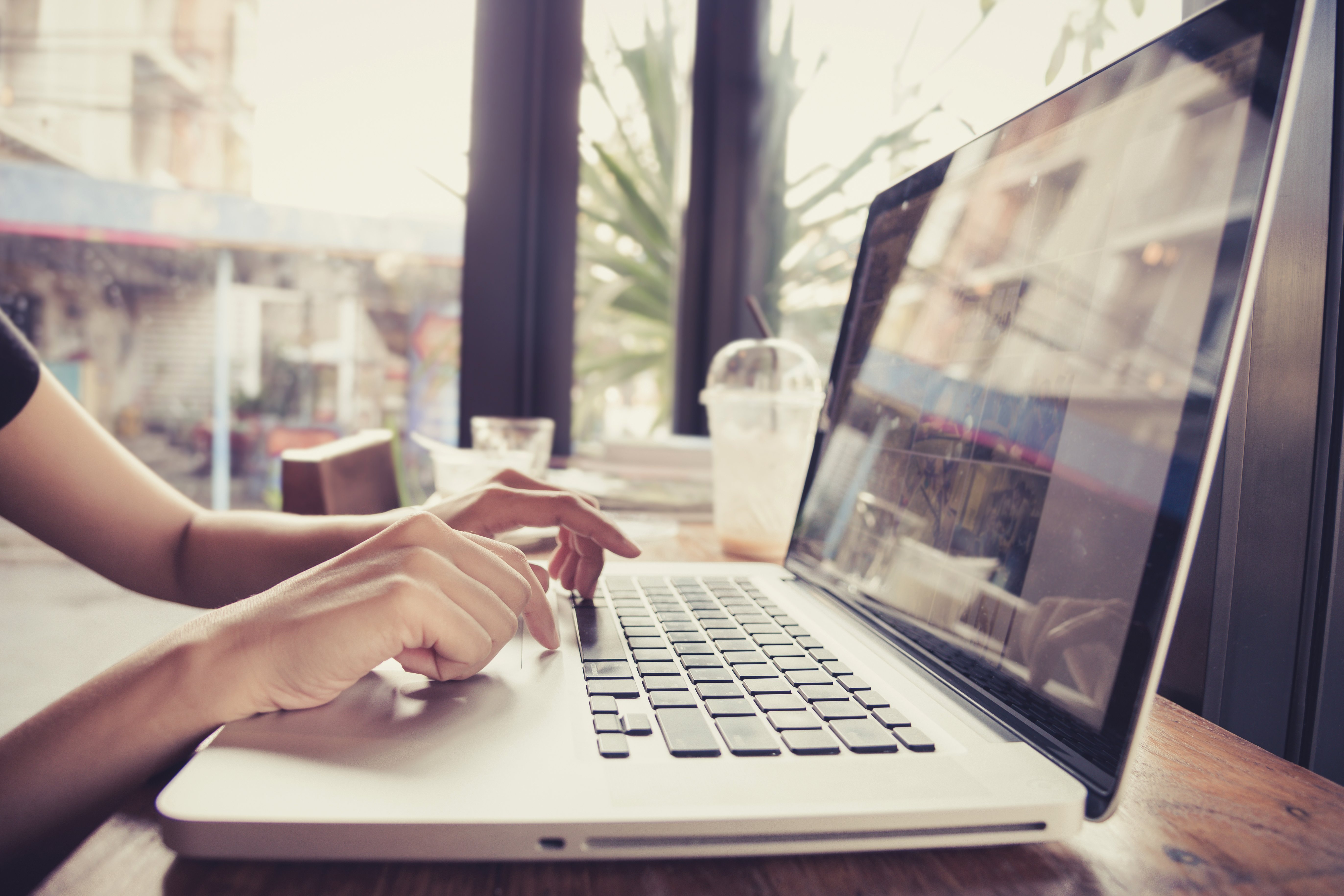 Person sitzt in einem Café an einem Laptop und tippt