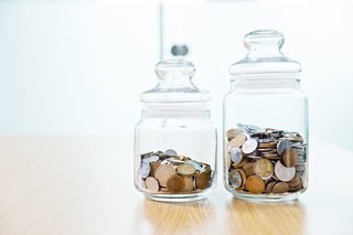 Geldmünzen in zwei verschiedenen Gefäßen aus Glas, die auf einem Tisch nebeneinander stehen.