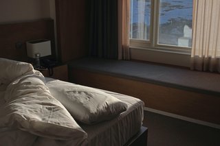 Mattes Licht fällt in ein Zimmer mit einem Bett, der Rest des Zimmers liegt im Dunkeln