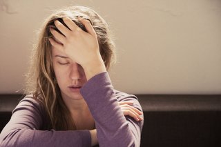 Junge, erschöpfte Frau stützt ihren Kopf mit geschlossenen Augen auf ihrer Hand auf