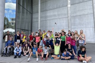 Das Foto zeigt die Teilnehmenden, Begleiterinnen und Begleiter sowie Tänzerin Barbara Galli-Jescheck und den Akkordeonspieler vor der Pinakothek der Moderne.