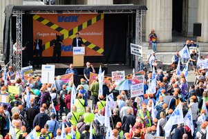 Auf einer B&uuml;hne mitten auf dem K&ouml;nigsplatz steht Hermann Imhof, Sprecher des Landesvorstands des VdK Bayern, hinter einem Rednerpult. Er spricht zu Hunderten Demonstrierenden und Fahnen und Plakate in die H&ouml;he halten.)