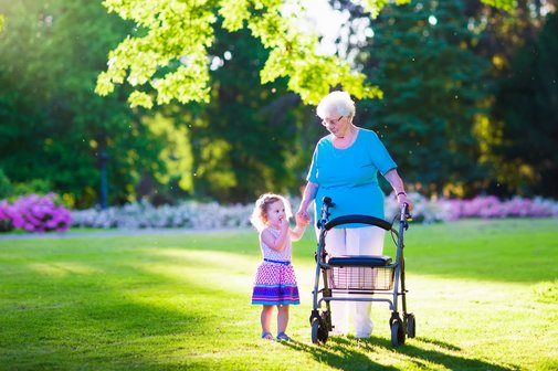 Auf dem Foto ist eine ältere Frau am Rollator mit einem kleinen Mädchen zu sehen.