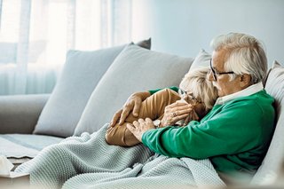 Ein älteres Ehepaar ruht sich, aneinander gekuschelt, auf dem Sofa aus.
