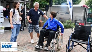Hans-Jürgen Wittig mit zwei interessierten Besuchern vor dem VdK-Stand auf dem Hessentag in Pfungstadt. Ein Jugendlicher sitzt in einem Rollstuhl. Er hate gerade den Sensibilisierungsparcours des VdK ausprobiert, um zu lernen, wie sich Rollstuhlnutzende Menschen fortbewegen und auf welche Hindernisse sie treffen.