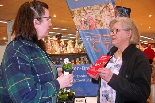 Eine Ehrenamtliche überreicht einer Besucherin eine Blume und einen Flyer.