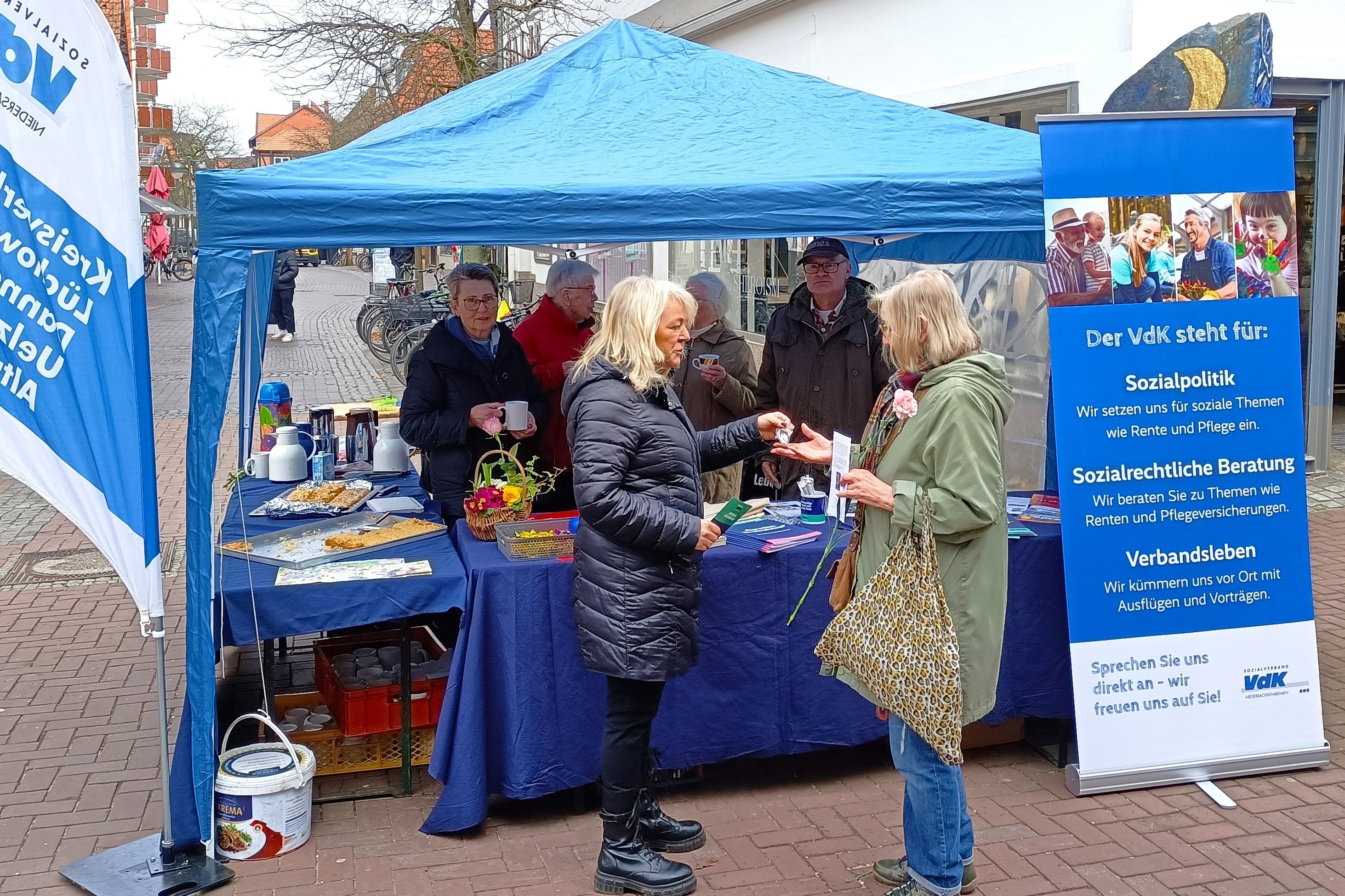 VdK-Ehrenamtliche zusammen mit Interessierten am blauen VdK-Infostand in Uelzen im März 2024