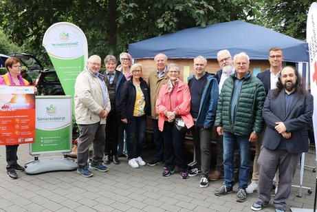 Eine Gruppe Menschen steht vor einem Informationsstand. Eine Dame links im Bild hält ein Plakat zum Thema Hitzeschutz in die Höhe.