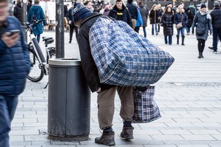 Ein alter Mann mit großen Taschen sucht im Mülleimer nach Pfandflaschen