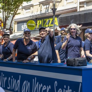 Frauen, Männer und Kinder winken von einem Festwagen mit der Aufschrift VdK.