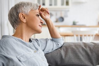 Eine Frau mit kurzen grauen Haaren blickt sorgenvoll und hält eine Hand vor den Kopf.