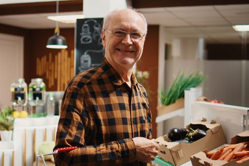 Ein älterer Herr steht vor einer Theke mit Obst- und Gemüse im Supermarkt.