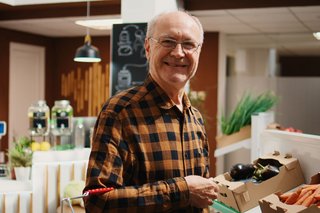 Ein älterer Herr steht vor einer Theke mit Obst- und Gemüse im Supermarkt.