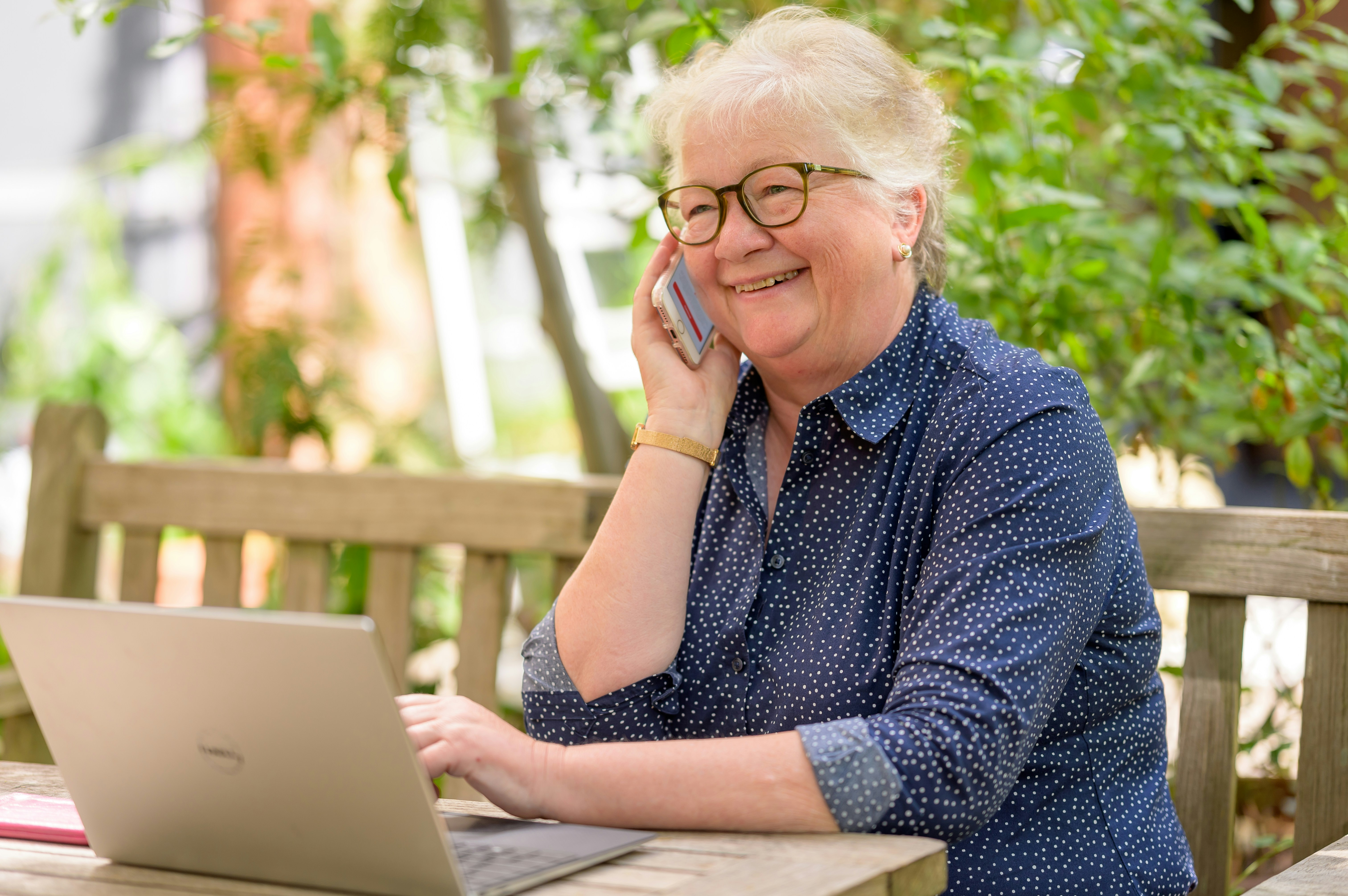 Seniorin am Smartphone, vor ihr ein aufgeklappter Laptop