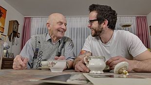 Symbolfoto: Älterer und junger Mann trinken gemeinsam Tee und lachen miteinander
