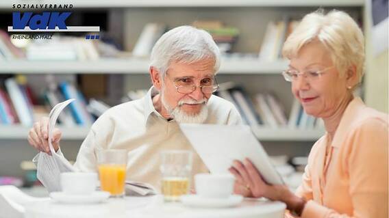 Eine Frau und ein Mann lesen gemeinsam am Tisch Zeitung. Er eine gedruckte Zeitung, sie liest am Tablet.