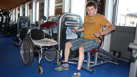 Marcel Thimmel trainiert seine Arme im Studio, der Rollstuhl steht daneben