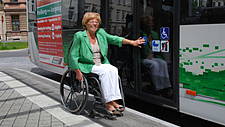 Rollstuhlfahrerin drückt die Türöffnungstaste an einer Bustür.