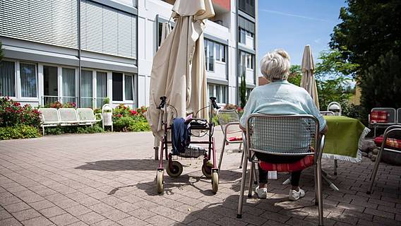 Symbolfoto: Ältere Frau sitzt vor einem Seniorenheim in der Sonne