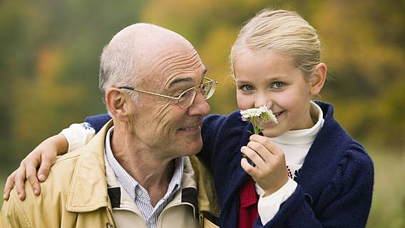 Symbolfoto: Enkelin und Opa Arm in Arm - sie riecht gerade an einer Blume