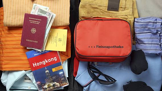 Symbolfoto: Gepackte Sachen für eine Reise - gefaltete Kleidung, eine Reiseapotheke und ein Reiseführer 