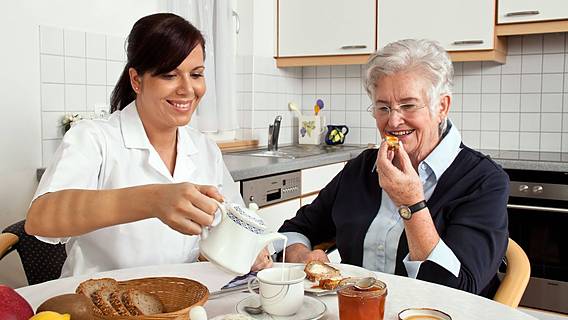 Eine Pflegerin und eine ältere Frau sitzen am Küchentisch und essen.