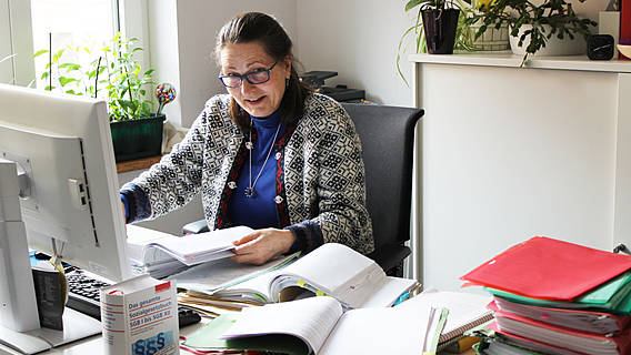 Foto: VdK-Rechtsanwältin Christine Akinci sitzt an ihrem Schreibtisch im Büro, um sie herum liegen Akten und Sozialgesetzbücher