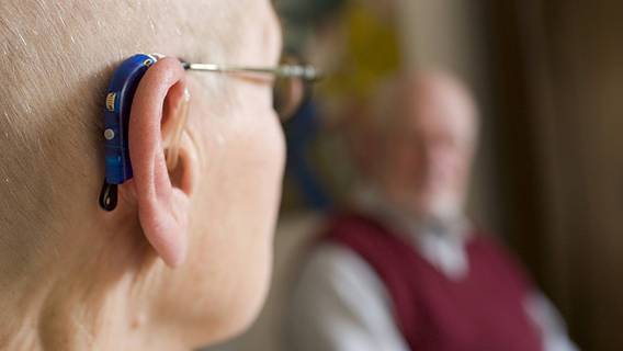 Ein alter Mann trägt ein blauen Hörgerät hinter seinem Ohr.