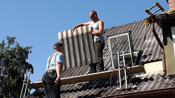 Zwei Bauarbeiter hantieren mit asbesthaltiger Dachpappe.