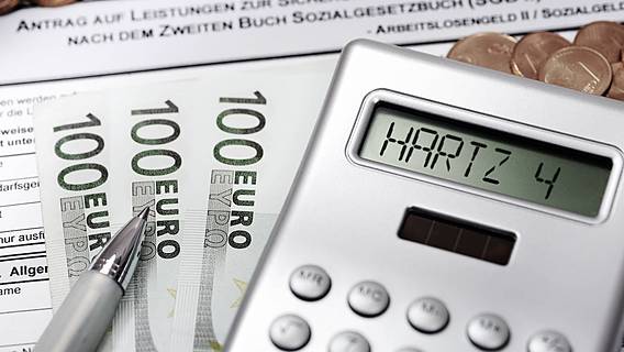 Symbolfoto: Ein Antrag auf Arbeitslosengeld 2, darauf liegen drei 100-Euro-Scheine, ein Kugelschreiber und ein Taschenrechner, auf dessen Display 